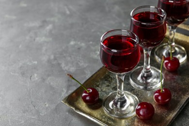 Delicious cherry liqueur in glasses and fresh berries on grey table, space for text