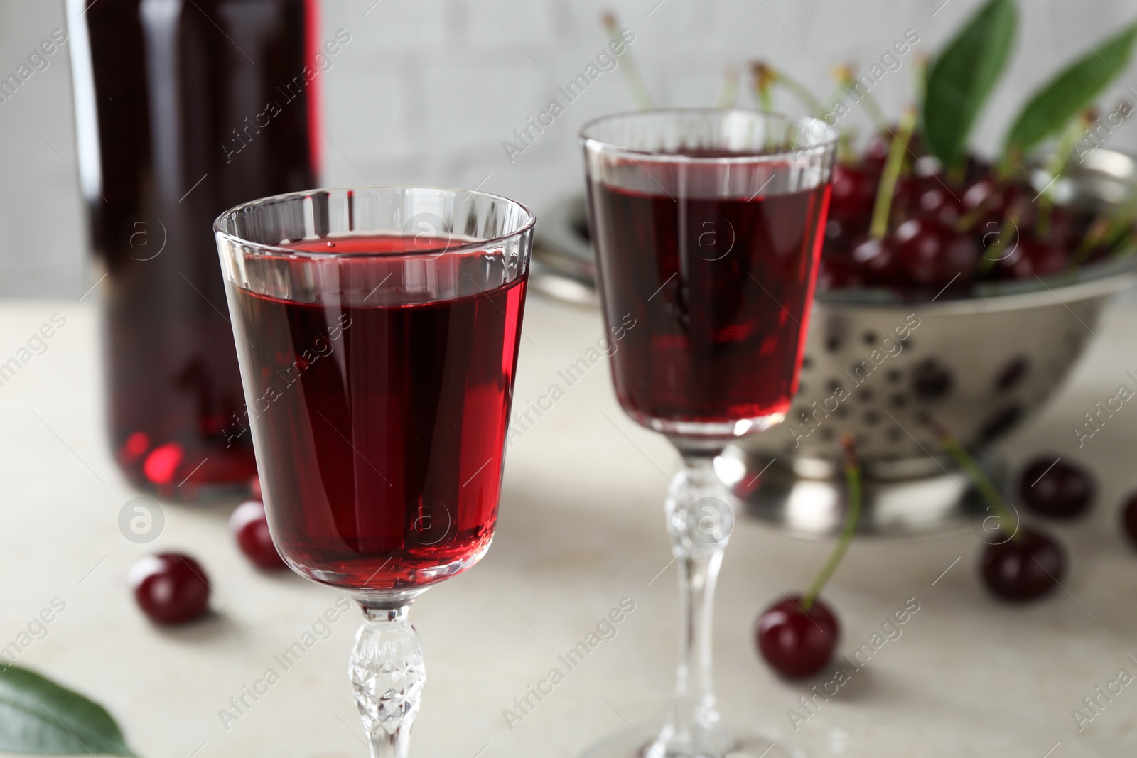 Photo of Delicious cherry liqueur in glasses and fresh berries on light grey table