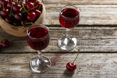 Photo of Delicious cherry liqueur in glasses and fresh berries on wooden table, space for text