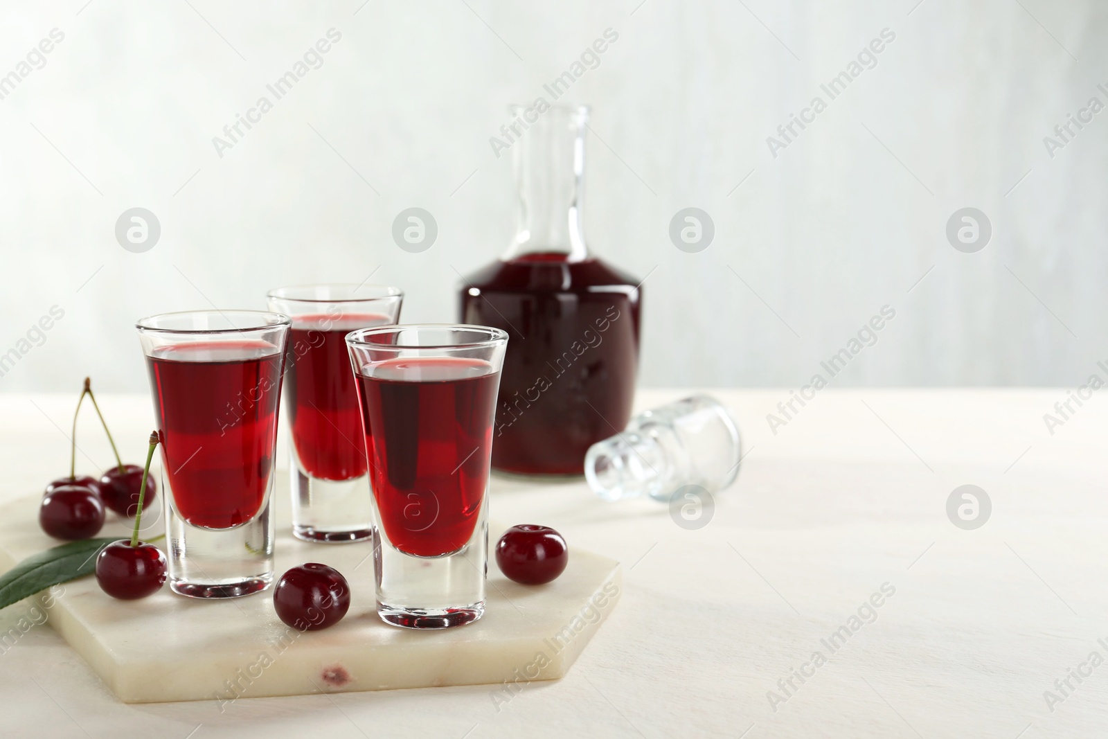 Photo of Delicious cherry liqueur and berries on white table. Space for text