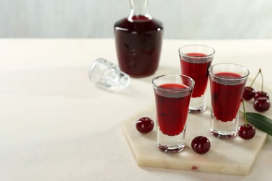 Photo of Delicious cherry liqueur and berries on white table. Space for text