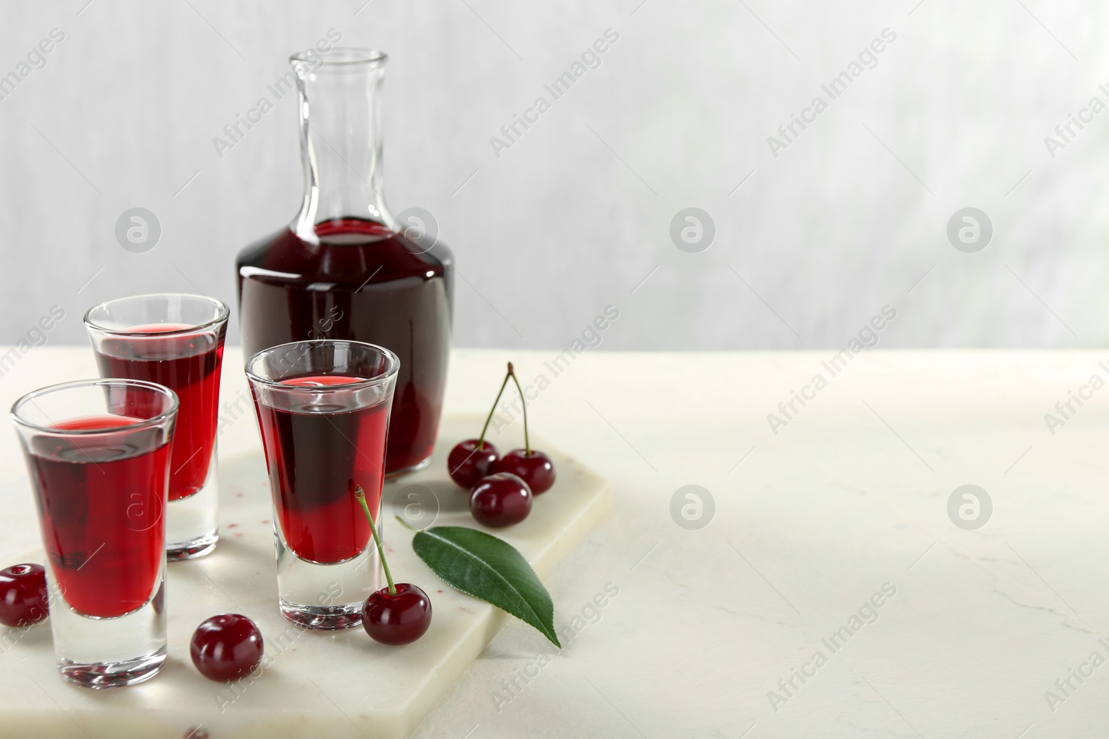 Photo of Delicious cherry liqueur and berries on white table. Space for text