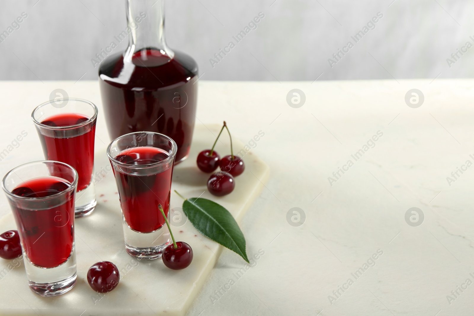 Photo of Delicious cherry liqueur and berries on white table. Space for text