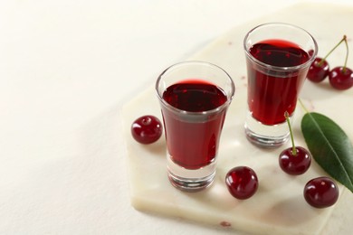 Photo of Delicious cherry liqueur in shot glasses and berries on white table, closeup. Space for text