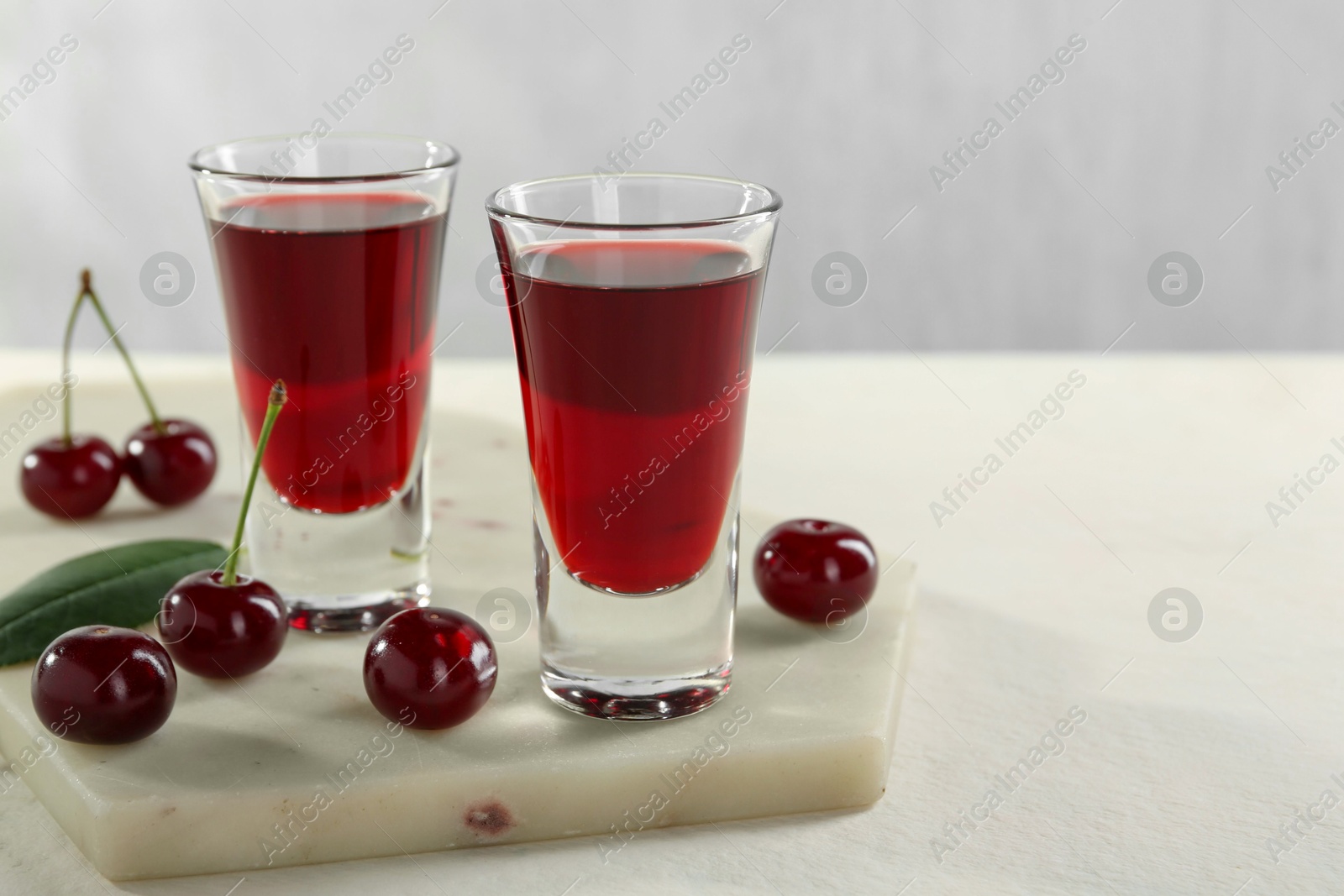 Photo of Delicious cherry liqueur in shot glasses and berries on white table, closeup. Space for text