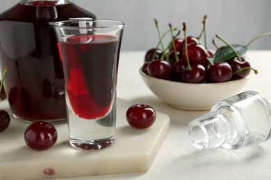 Photo of Delicious cherry liqueur and berries on white table, closeup