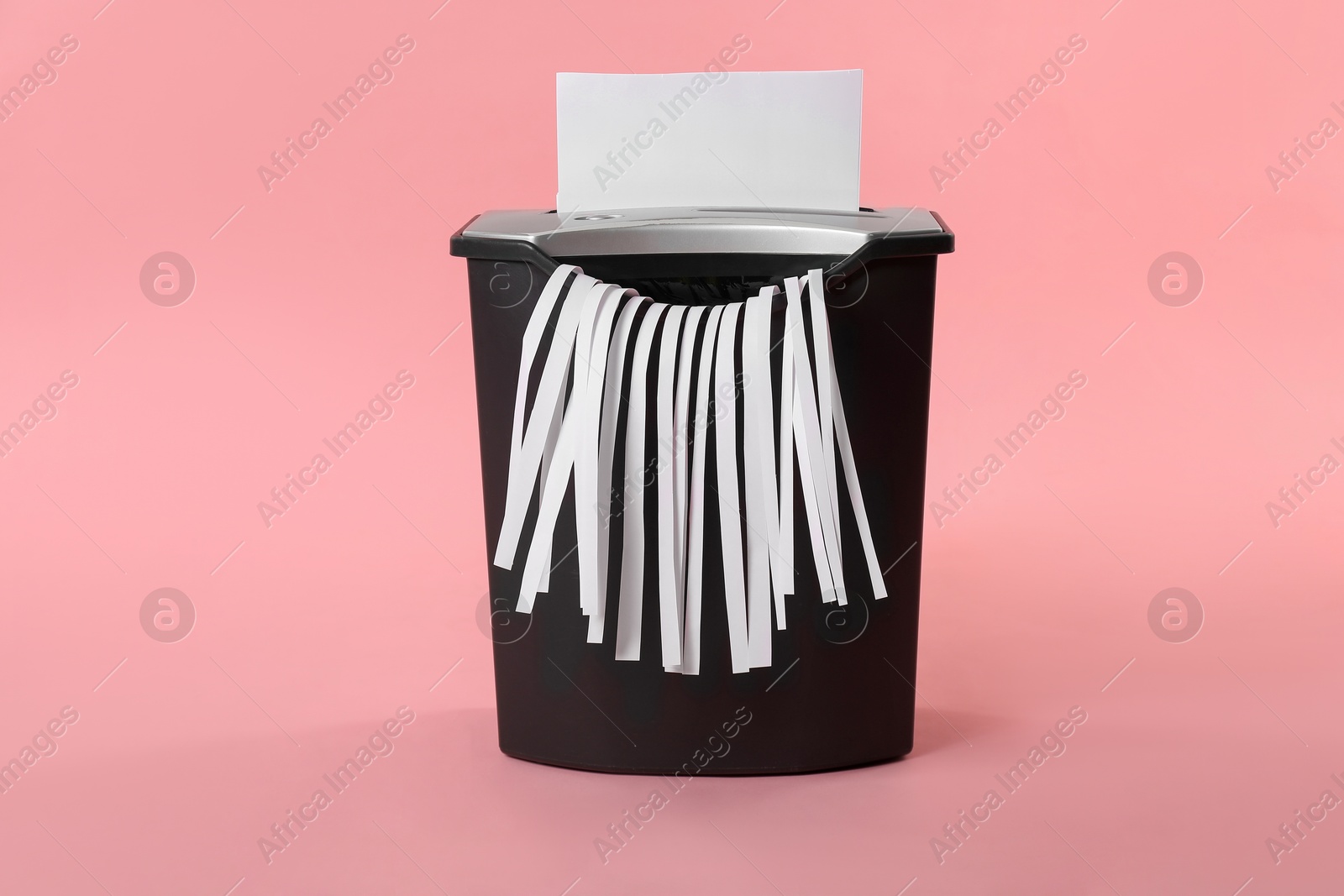 Photo of Destroying sheet of paper with shredder on pink background