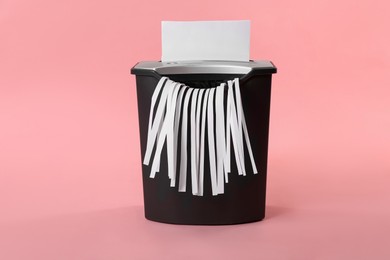 Destroying sheet of paper with shredder on pink background