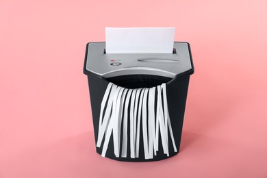 Photo of Destroying sheet of paper with shredder on pink background