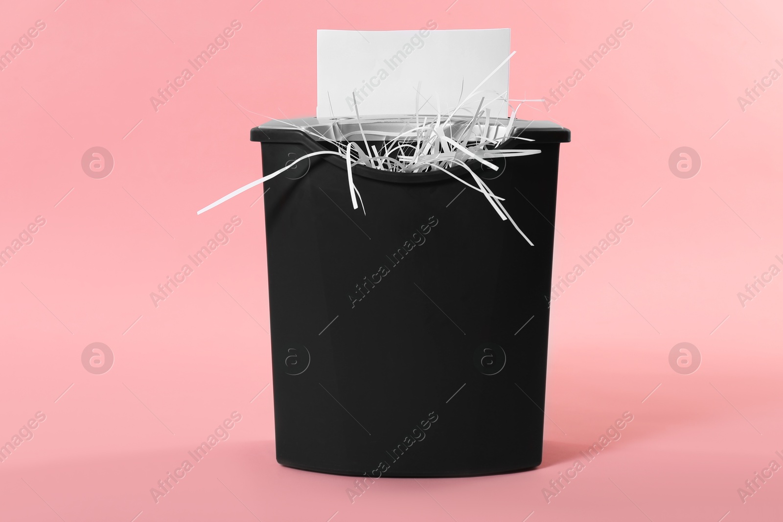 Photo of Destroying sheet of paper with shredder on pink background