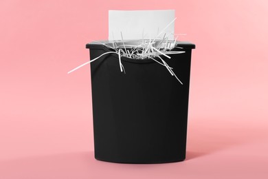 Photo of Destroying sheet of paper with shredder on pink background