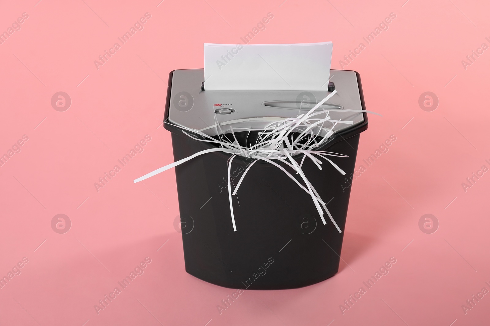 Photo of Destroying sheet of paper with shredder on pink background