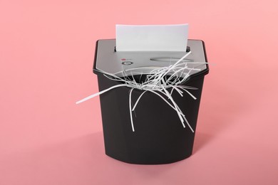 Photo of Destroying sheet of paper with shredder on pink background