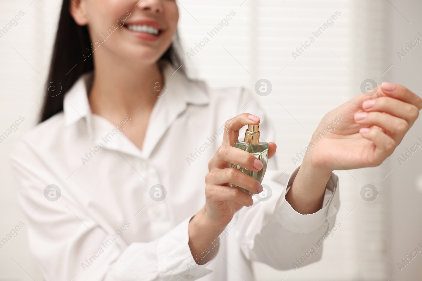 Photo of Smiling woman spraying perfume onto wrist at home, closeup