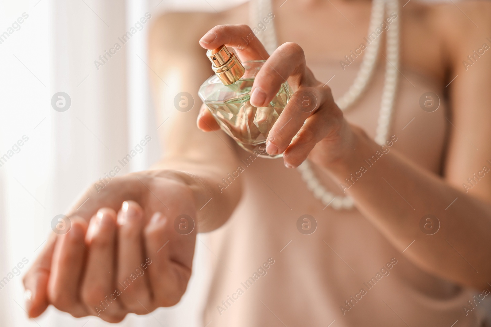 Photo of Woman spraying perfume onto wrist indoors, closeup