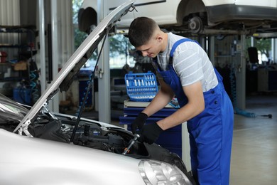 Young auto mechanic fixing car at automobile repair shop