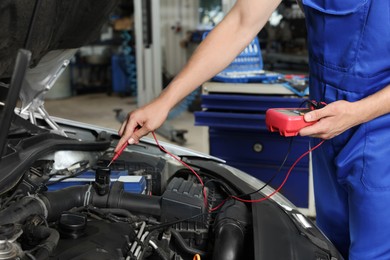 Photo of Auto mechanic with multimeter doing diagnostic at automobile repair shop, closeup