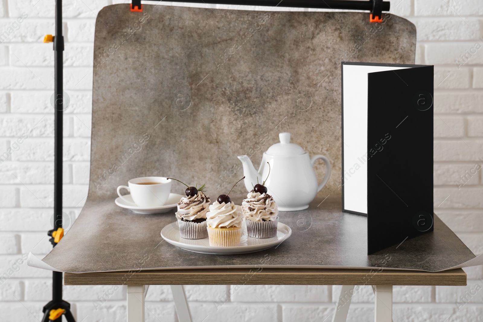 Photo of Cupcakes, tea and light reflector on table in studio. Professional food photography