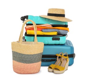 Photo of Bright suitcases with clothes, wicker hat, bag and shoes isolated on white