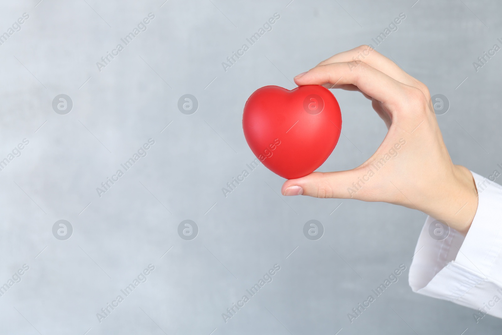 Photo of Woman holding red heart on grey background, closeup. Space for text