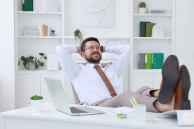 Smiling businessman with hands behind his head holding legs on table in office. Break time