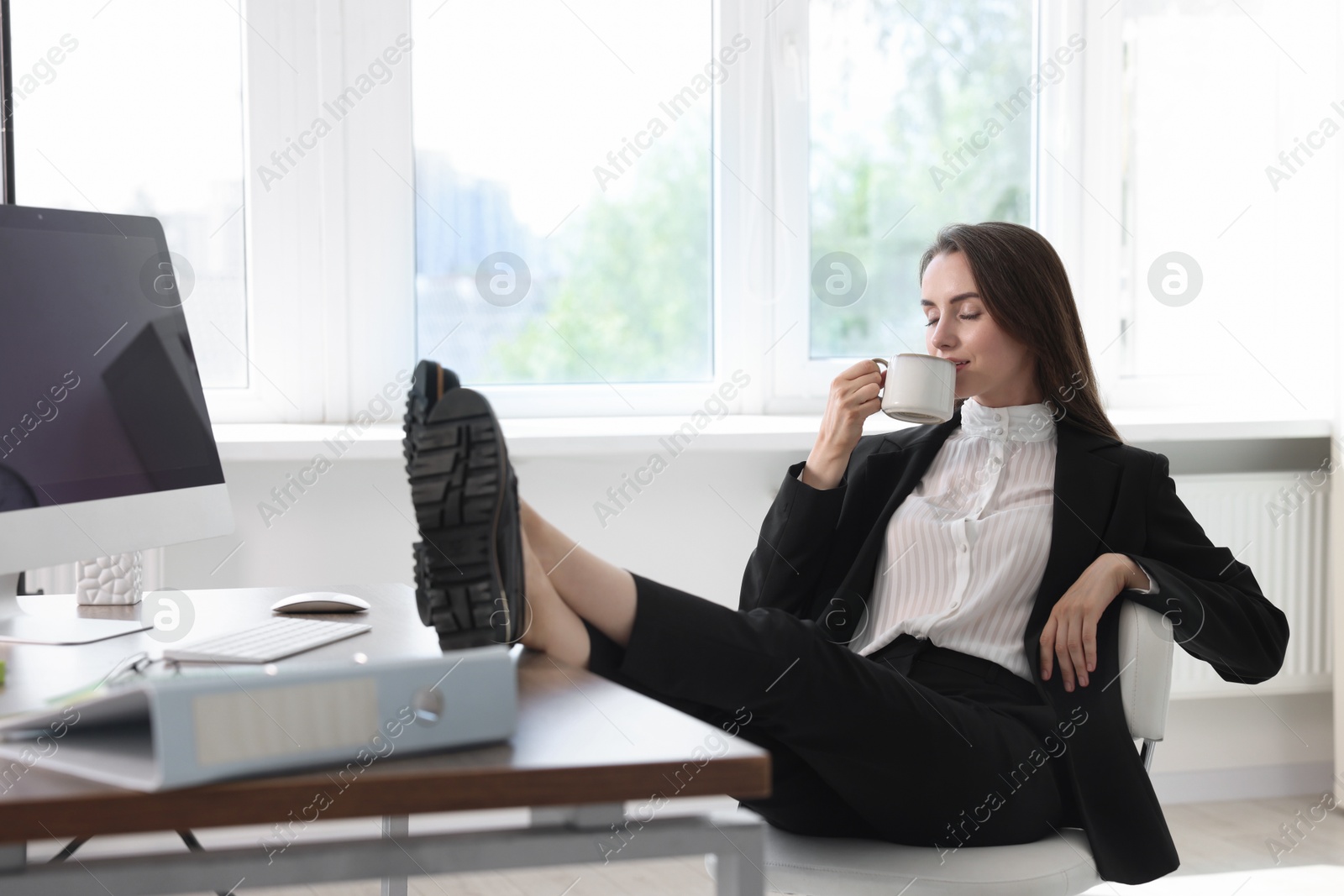 Photo of Businesswoman drinking coffee holding legs on table in office. Break time