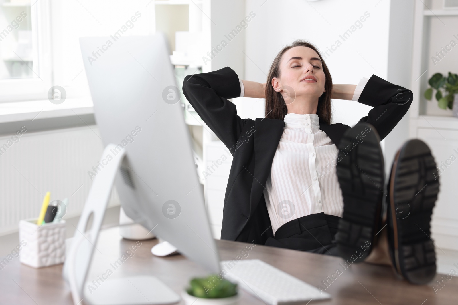 Photo of Smiling businesswoman with hands behind her head holding legs on table in office. Break time