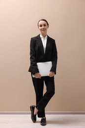 Smiling businesswoman with laptop near beige wall