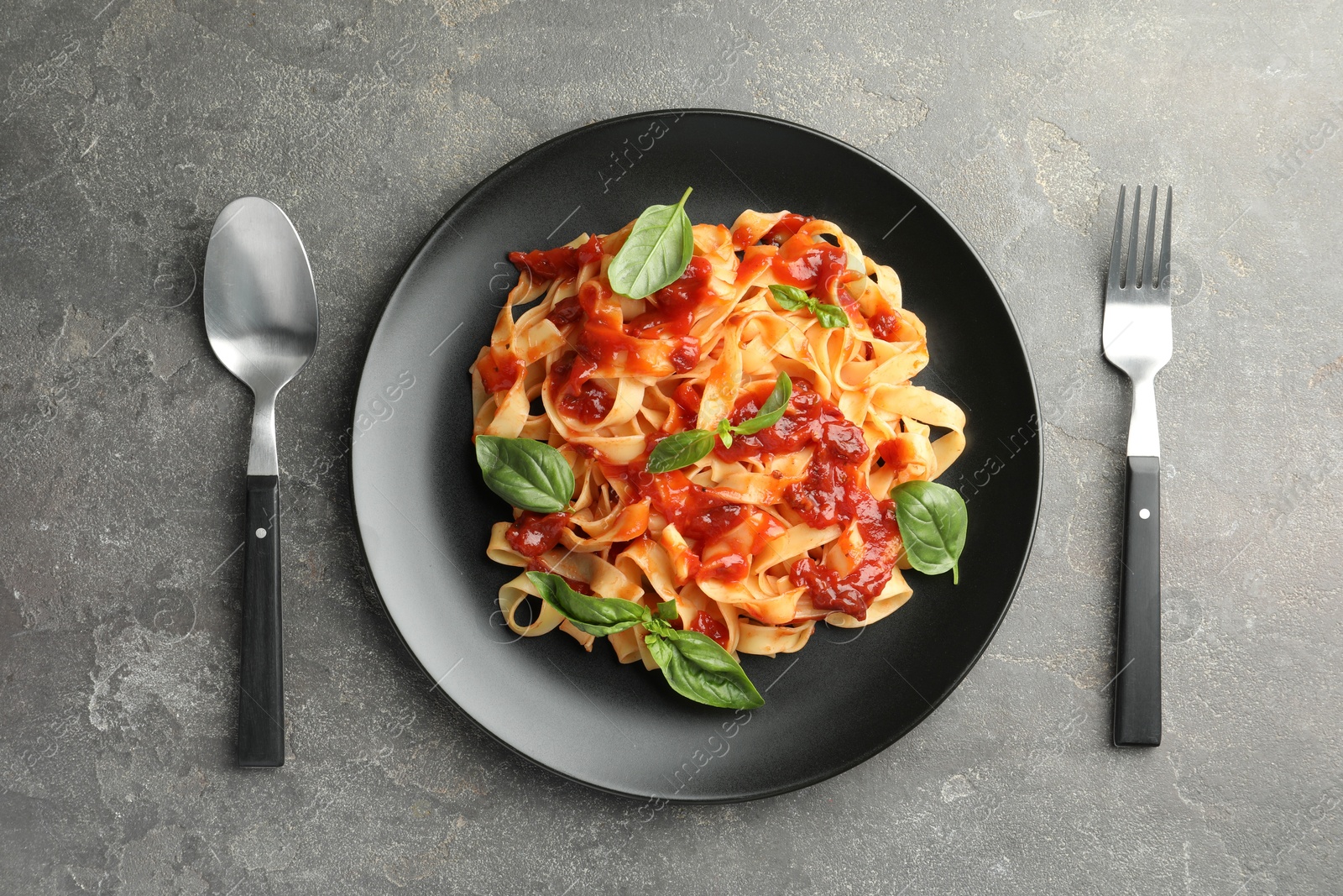 Photo of Delicious pasta with tomato sauce and basil served on grey textured table, flat lay