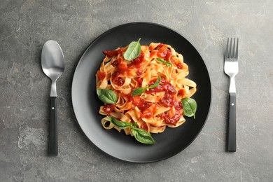 Delicious pasta with tomato sauce and basil served on grey textured table, flat lay