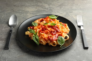 Photo of Delicious pasta with tomato sauce and basil served on grey textured table, closeup