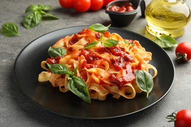 Photo of Delicious pasta with tomato sauce and basil on grey textured table, closeup