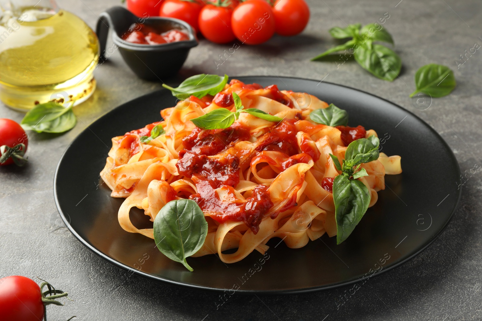 Photo of Delicious pasta with tomato sauce and basil on grey textured table, closeup