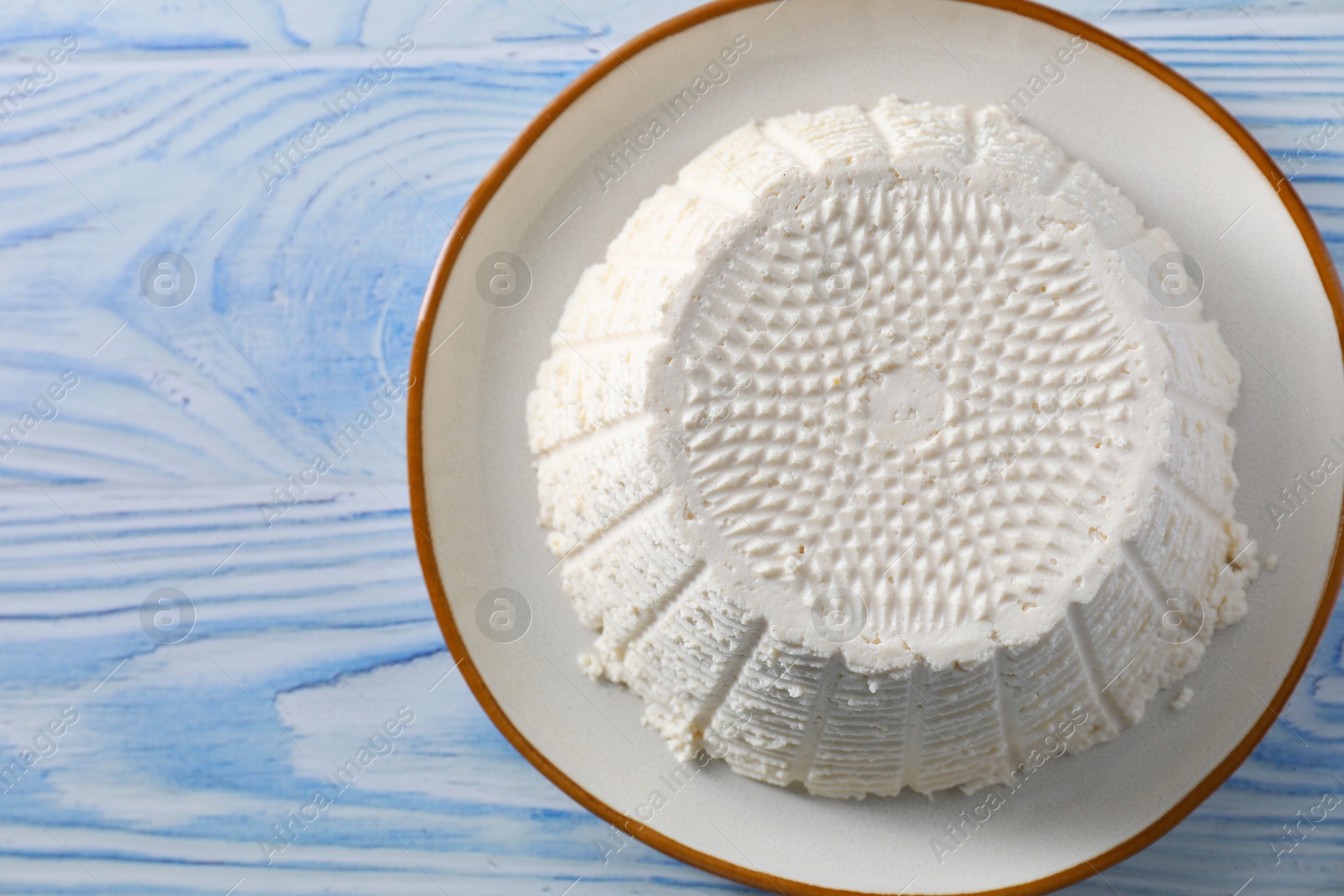 Photo of Tasty ricotta (cream cheese) on light blue wooden table, top view. Space for text