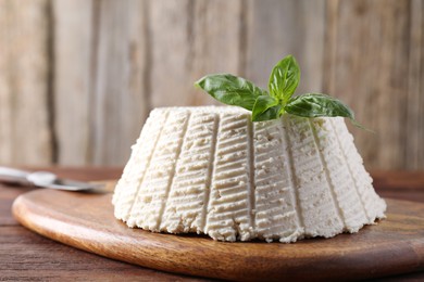 Photo of Tasty ricotta (cream cheese), basil and knife on wooden table, closeup