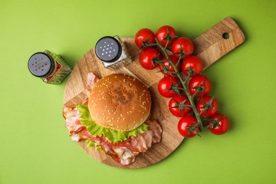 Photo of Delicious burger with bacon, tomatoes and lettuce on green background, top view