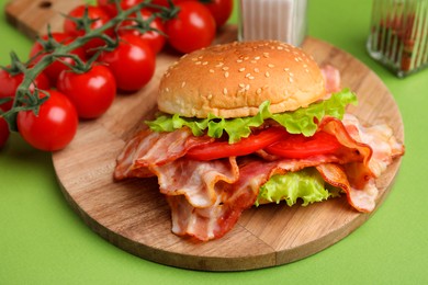 Photo of Delicious burger with bacon, tomatoes and lettuce on green background