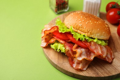 Photo of Delicious burger with bacon, tomato and lettuce on green background, space for text