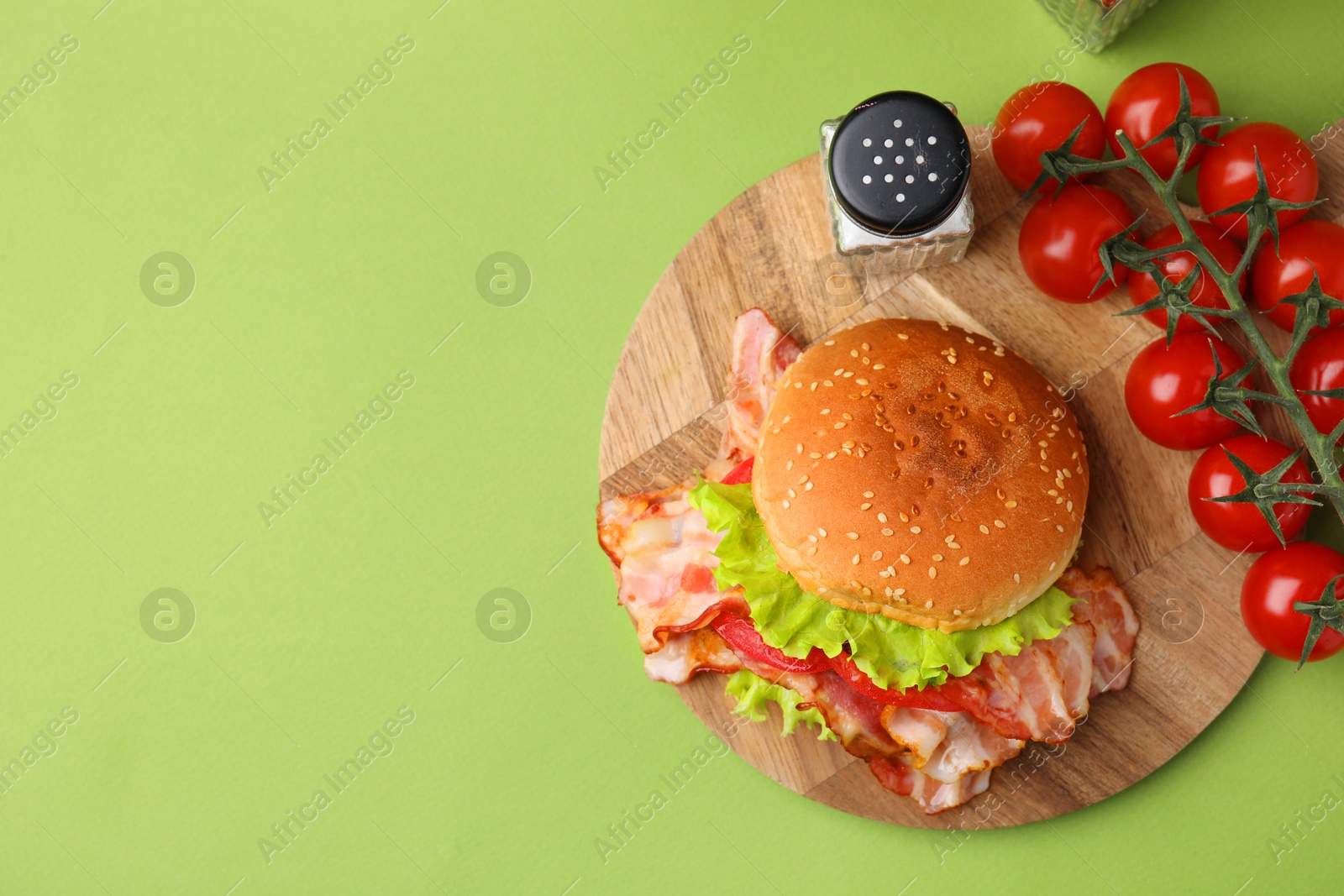 Photo of Delicious burger with bacon, tomatoes and lettuce on green background, top view. Space for text