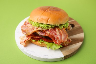 Photo of Delicious burger with bacon, patty and tomato on green background