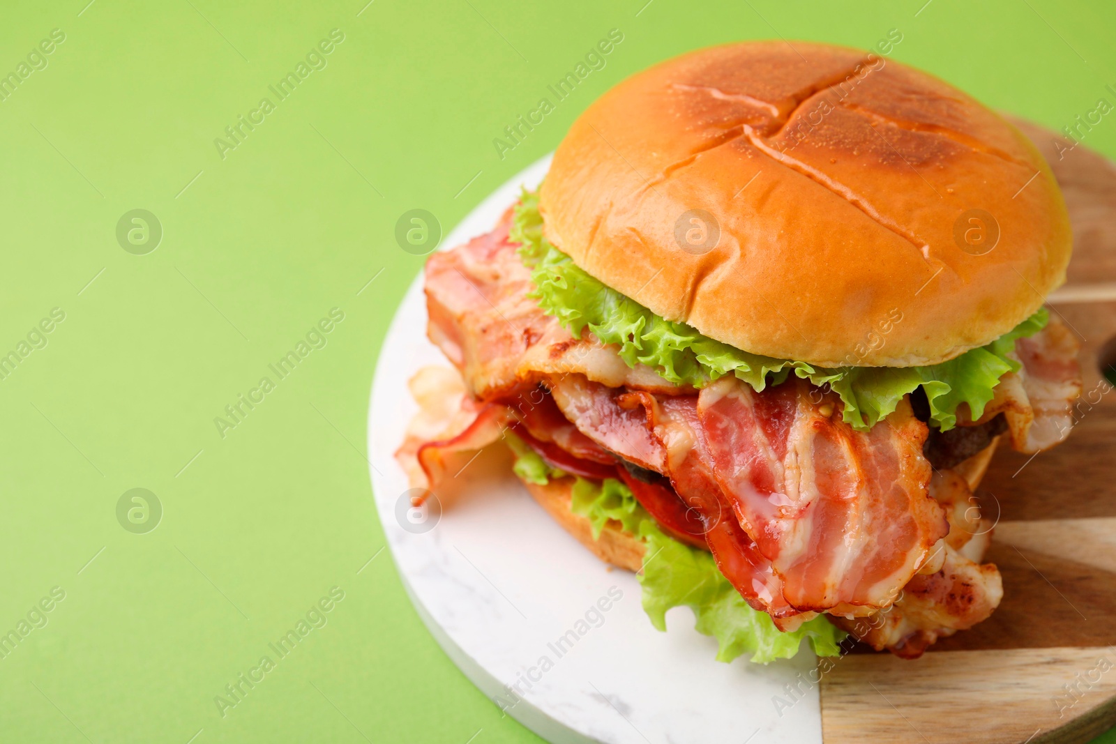 Photo of Delicious burger with bacon and lettuce on green background, space for text