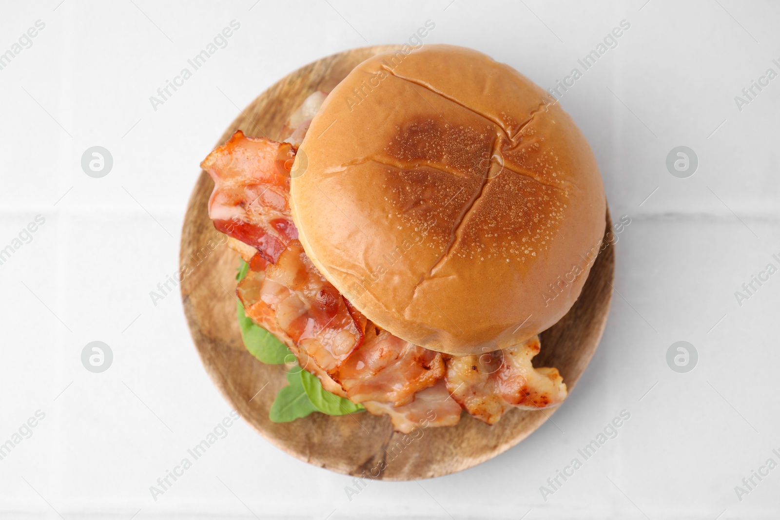 Photo of Delicious burger with bacon and greens on white tiled table, top view