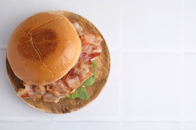 Photo of Delicious burger with bacon and greens on white tiled table, top view. Space for text