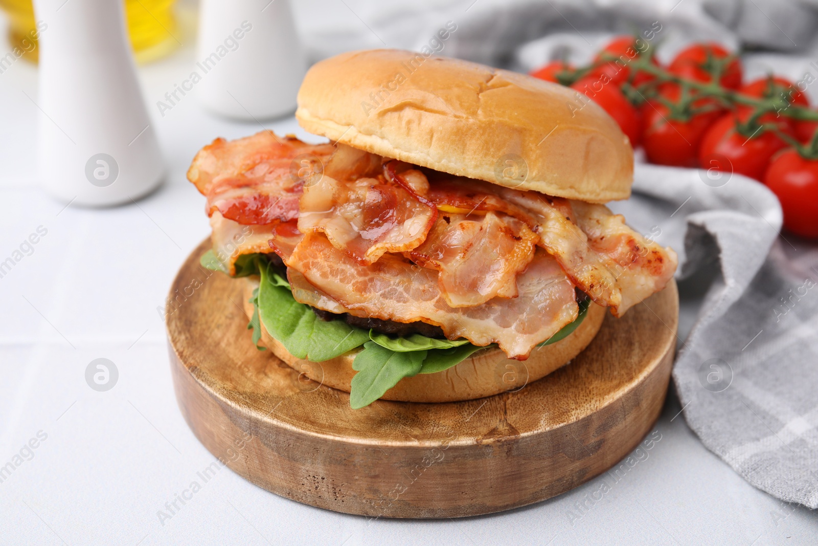 Photo of Delicious burger with bacon and greens on light table, closeup