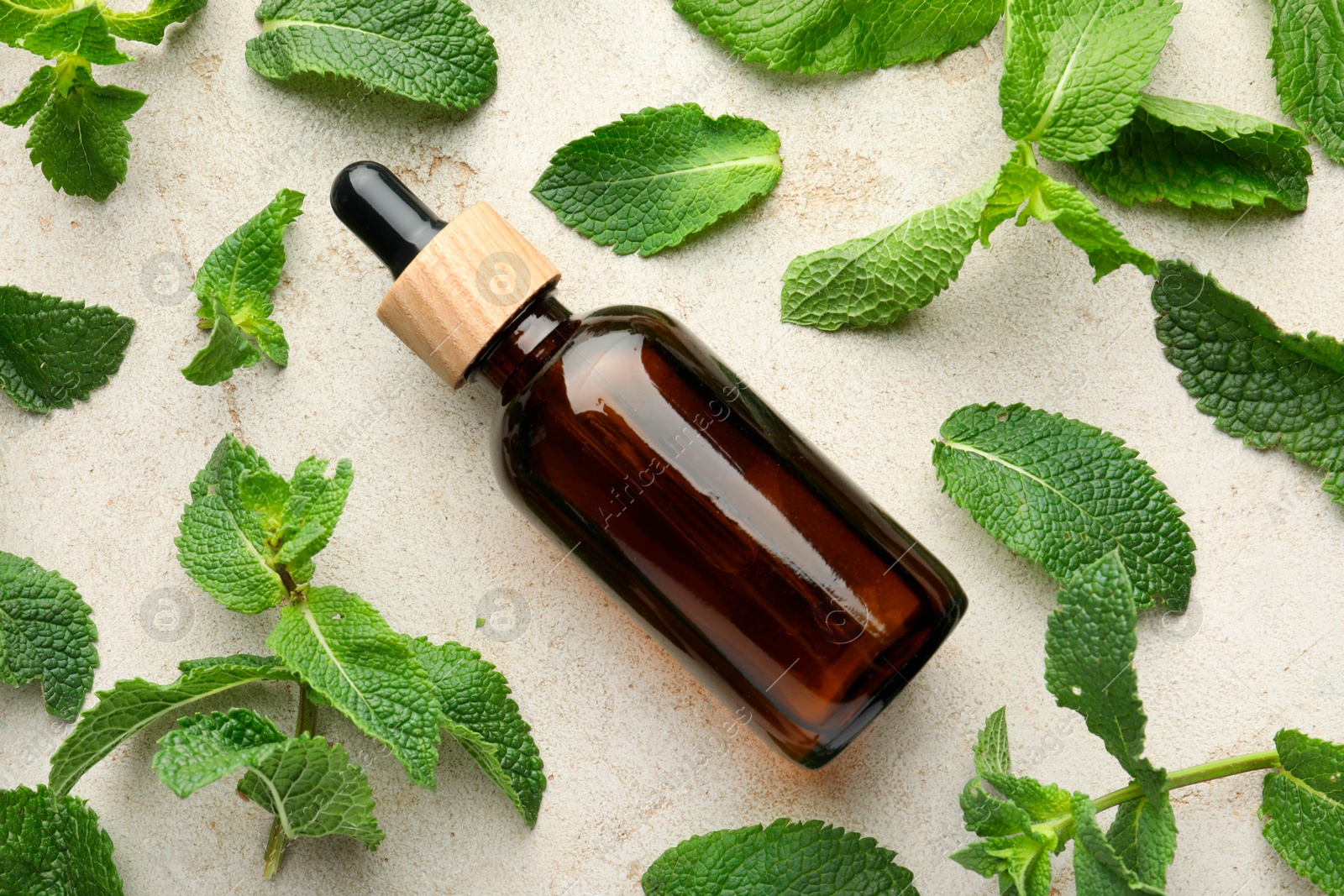 Photo of Bottle of essential oil and mint on light textured table, flat lay