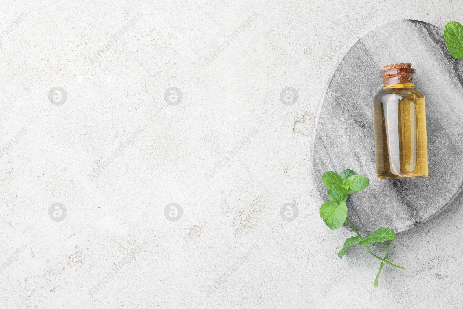 Photo of Bottle of essential oil and mint on light textured table, top view. Space for text