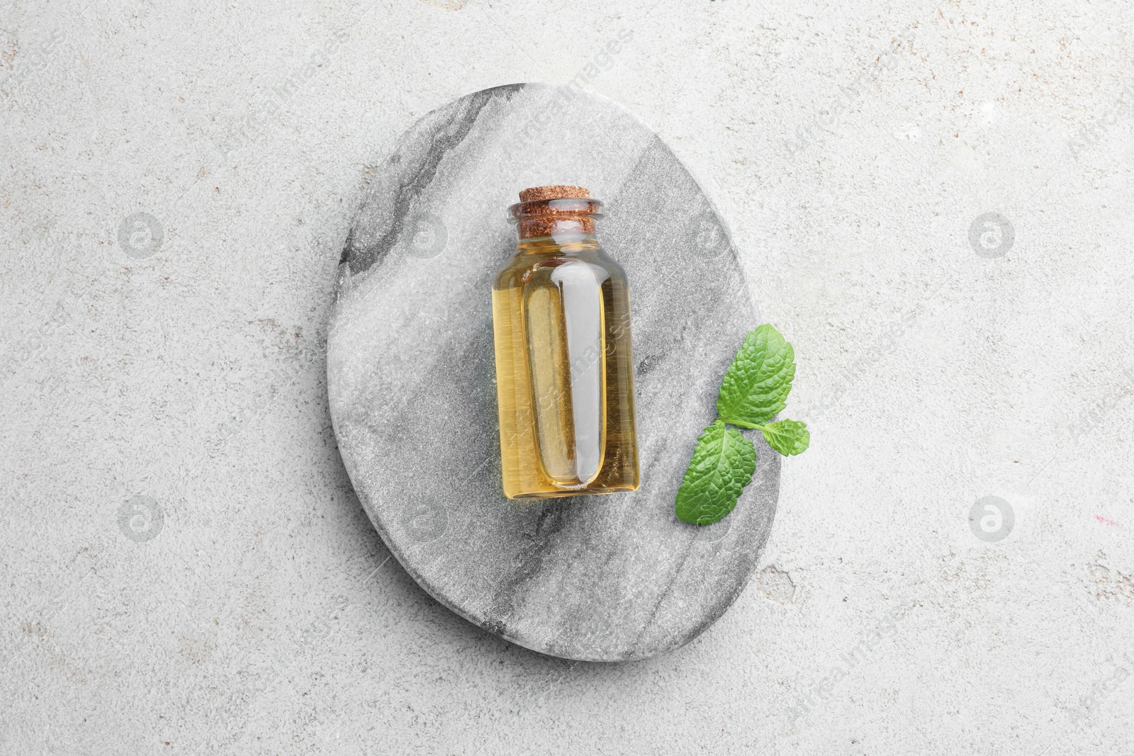 Photo of Bottle of essential oil and mint on light textured table, top view