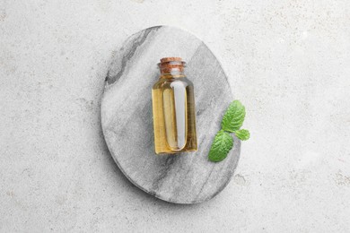 Photo of Bottle of essential oil and mint on light textured table, top view