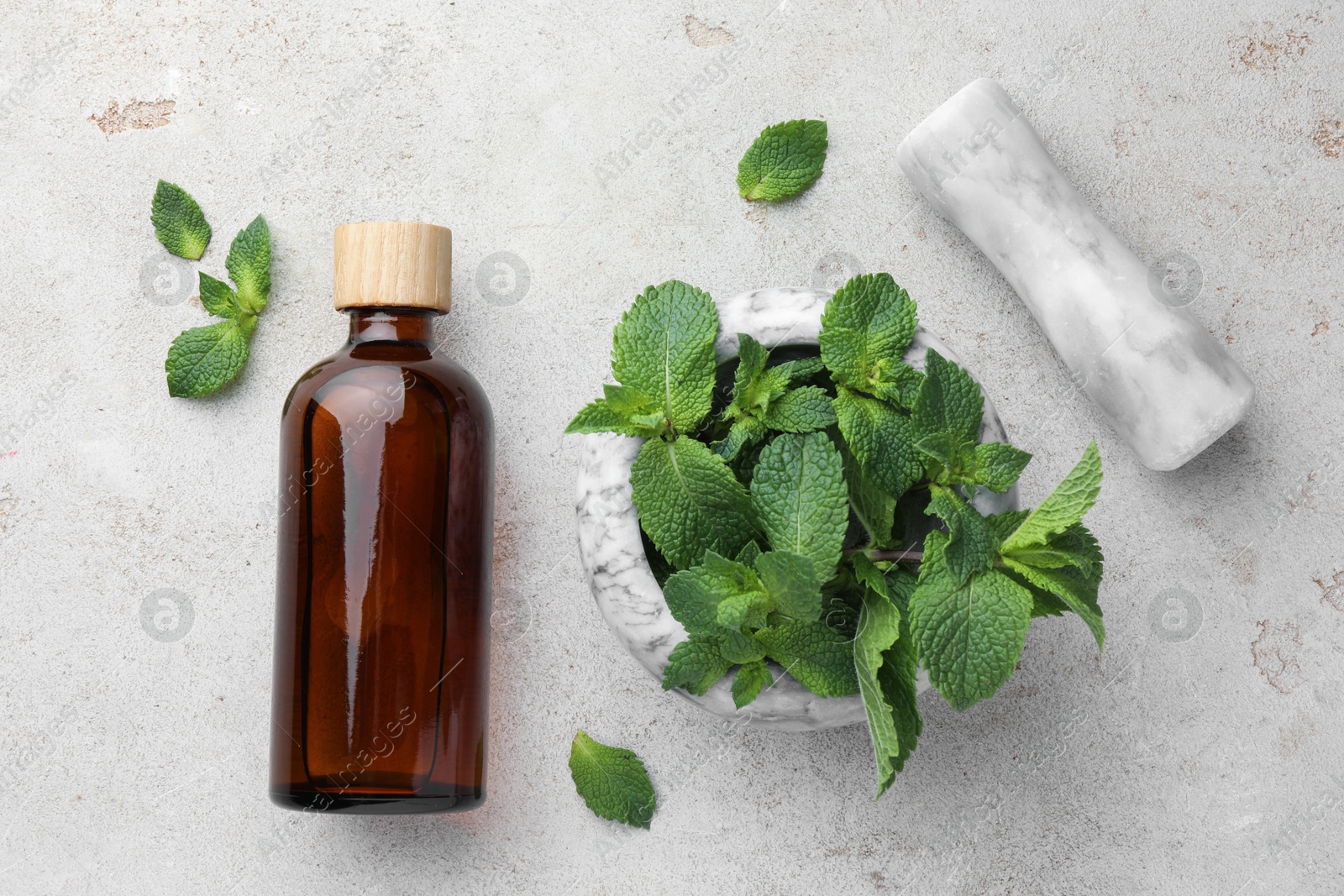 Photo of Bottle of essential oil, mint, mortar and pestle on light textured table, flat lay