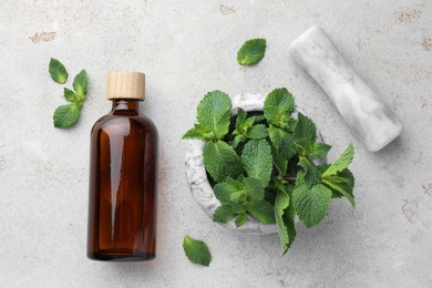 Photo of Bottle of essential oil, mint, mortar and pestle on light textured table, flat lay